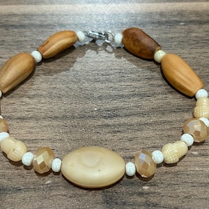 May include: A beaded bracelet featuring a variety of natural-toned beads. The bracelet includes light brown, tan, and faceted beads, along with small white beads. The bracelet is secured with a silver clasp. A jewelry item.