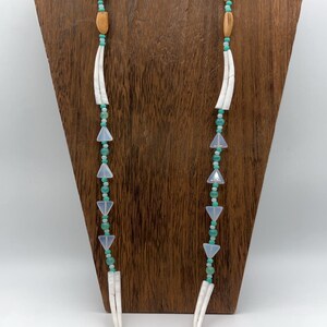 May include: A long necklace with a variety of beads, including light brown wooden beads, white tube beads, and turquoise-colored beads. The necklace also features triangular, iridescent beads and a silver-colored clasp.