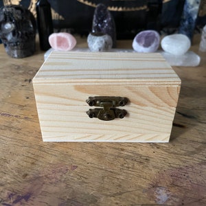 May include: A small wooden box with a hinged lid and a brass latch. The box is made of light-colored wood with a natural grain pattern.
