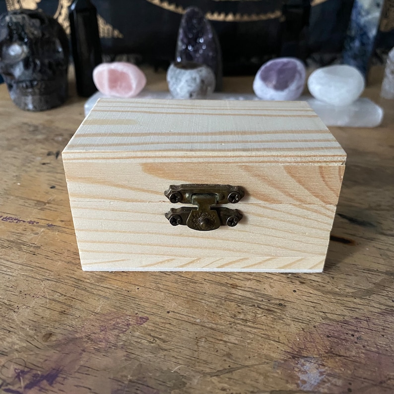 May include: A small wooden box with a hinged lid and a brass latch. The box is made of light-colored wood with a natural grain pattern.