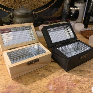 May include: Two wooden boxes with mirrored interiors. One box is natural wood and the other is black. Both boxes have a small metal latch.