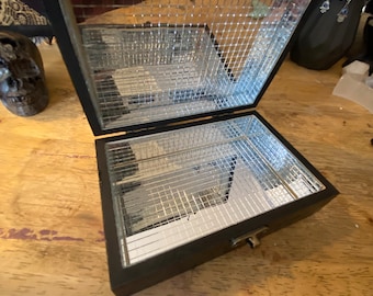 May include: A black wooden box with a mirrored interior. The box has a hinged lid and a latch. The mirror is divided into sections by a grid pattern.
