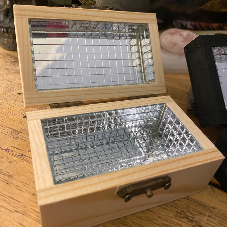 May include: A small wooden box with a hinged lid and a metal latch. The box is lined with a silver wire mesh.