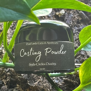 May include: A black jar with a label that reads "Dead Lands Curio & Apothecary Casting Powder Sigils-Circles-Dusting 0.5 oz". The jar is sitting on a bed of brown mulch.