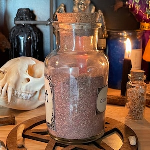 May include: A glass jar with a cork lid filled with a purple powder. The jar is labeled "Custom Blend". The jar is sitting on a wooden pentagram.