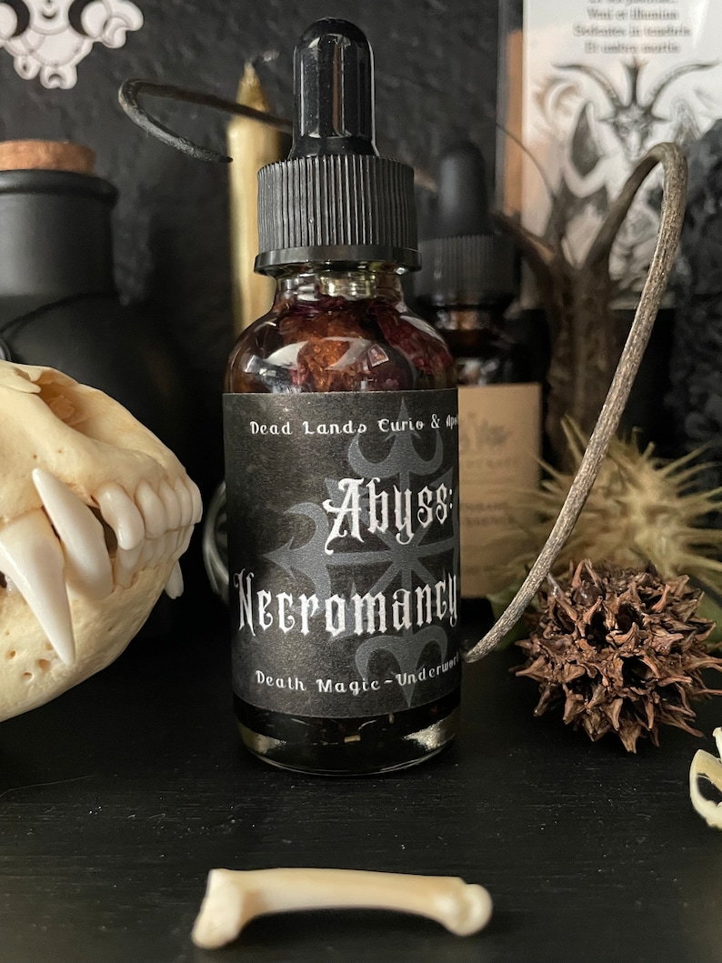 May include: A small glass bottle with a black dropper top and a black label. The label reads "Dead Lands Curio & Apothecary Abyss Necromancy Death Magic - Underworld".