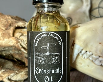 May include: A small glass bottle with a black cap and a black label that reads "Dead Lands Apothecary Crossroads Oil". The label features a black and white illustration of a crossroads with a signpost.