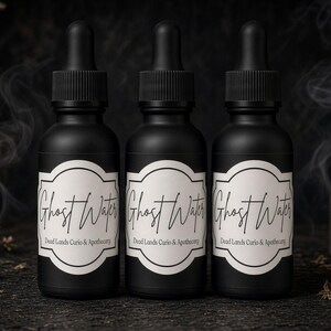 May include: Three matte black dropper bottles with white labels featuring the text Ghost Water and Dead Lands Curio & Apothecary. Each bottle has a black dropper cap and is arranged in a row against a dark background with wisps of smoke.