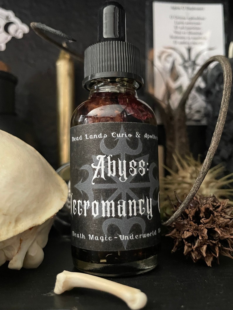 May include: A small glass bottle with a black dropper top and a black label. The label reads "Dead Lands Curio & Apothecary Abyss: Necromancy Oil Death Magic - Underworld"
