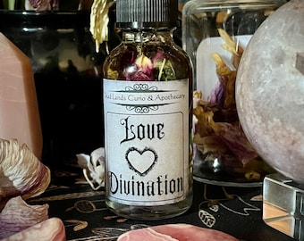 May include: A clear glass bottle with a black dropper top filled with a pink liquid and dried flowers. The label reads "Dead Lands Curio & Apothecary Love Divination".