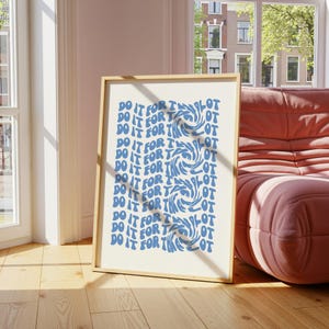 May include: A framed art print with the words "DO IT FOR THE LOT" in blue, repeated vertically. The artwork features three swirling designs in the center. The frame is a light wood color, and the print is displayed on a wooden floor.