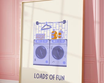 Op de afbeelding: Een ingelijste print met een illustratie over wasgoed. Het kunstwerk toont twee wasmachines, wasmiddelen en de tekst "LOADS OF FUN". Het kleurenschema omvat paarse, oranje en crèmetinten, wat een vrolijke uitstraling creëert.