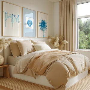 May include: A bedroom scene featuring a bed with beige bedding and pillows. Above the bed, three framed art prints depict a blue bikini, a seashell stamp, and a palm tree. The room has a neutral color palette with a window and beige curtains.