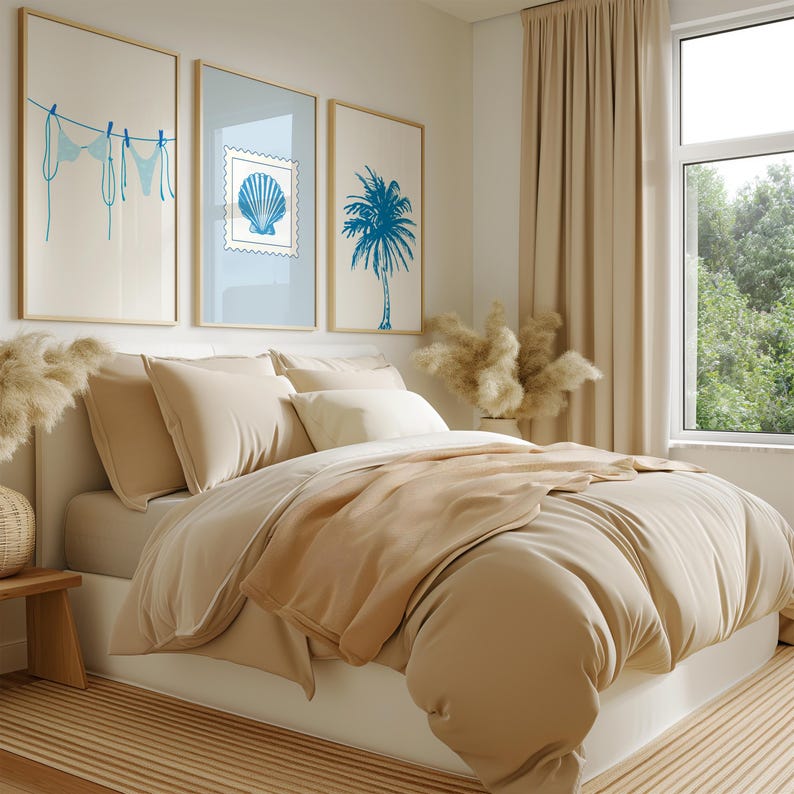 May include: A bedroom scene featuring a bed with beige bedding and pillows. Above the bed, three framed art prints depict a blue bikini, a seashell stamp, and a palm tree. The room has a neutral color palette with a window and beige curtains.