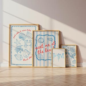 May include: A collection of framed art prints with a beach theme. The prints feature blue and white illustrations of seashells, starfish, and other marine life. Some prints include text such as "good vibes & ocean tides" and "meet me at the beach". The frames are a light wood color.