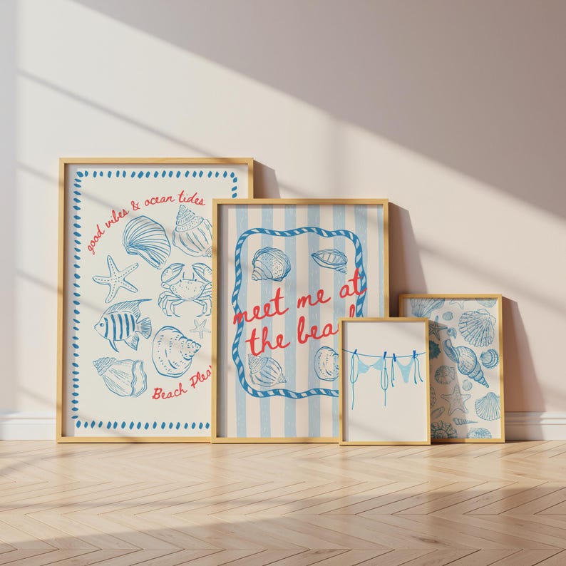 May include: A collection of framed art prints with a beach theme. The prints feature blue and white illustrations of seashells, starfish, and other marine life. Some prints include text such as "good vibes & ocean tides" and "meet me at the beach". The frames are a light wood color.