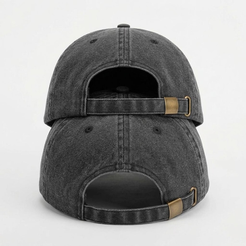 May include: Two dark gray baseball caps stacked on top of each other. The caps have a distressed, worn look. Each cap has a curved brim and an adjustable strap with a brass-colored buckle on the back.