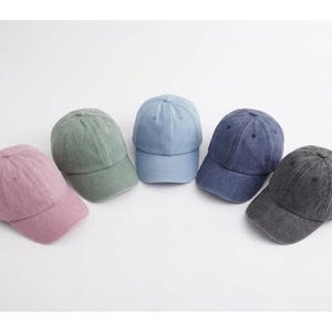 May include: Five baseball caps in various colors: dusty rose, sage green, light blue, navy blue, and charcoal gray. Each cap has a curved brim and a classic six-panel design, perfect for casual wear.