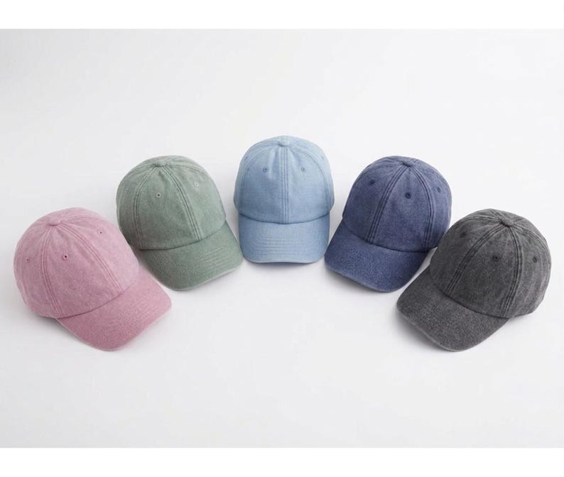 May include: Five baseball caps in various colors: dusty rose, sage green, light blue, navy blue, and charcoal gray. Each cap has a curved brim and a classic six-panel design, perfect for casual wear.