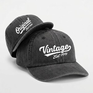 May include: Two dark gray baseball caps. One cap has the word "Original" and "Est. 2025" in white script. The other cap has the word "Vintage" and "Est. 1991" in white script.