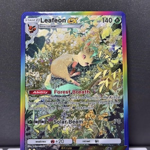 Puede incluir: Una carta coleccionable Pokémon Leafeon ex holográfica. La carta presenta un personaje Leafeon marrón y verde en un entorno forestal. La carta tiene un borde arcoíris y el texto "Forest Breath" y "Solar Beam".