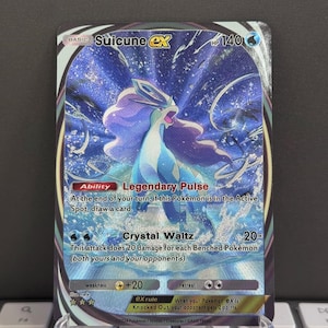 Könnte beinhalten: Eine Pokémon-Sammelkarte mit Suicune ex in Blau- und Lilatönen. Die Karte zeigt eine Suicune-Illustration mit den Texten "Legendary Pulse" und "Crystal Waltz". Die Karte wird auf einem transparenten Ständer präsentiert.