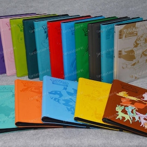 May include: A collection of colorful Pokemon card binders. The binders are in various colors, including purple, pink, green, blue, red, and brown. Some binders feature embossed designs and illustrations of Pokemon characters.