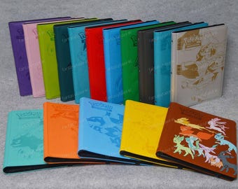 Può includere: Una collezione di raccoglitori di carte Pokémon colorati. I raccoglitori sono in vari colori, tra cui viola, rosa, verde, blu, rosso e marrone. Alcuni raccoglitori presentano disegni in rilievo e illustrazioni di personaggi Pokémon.