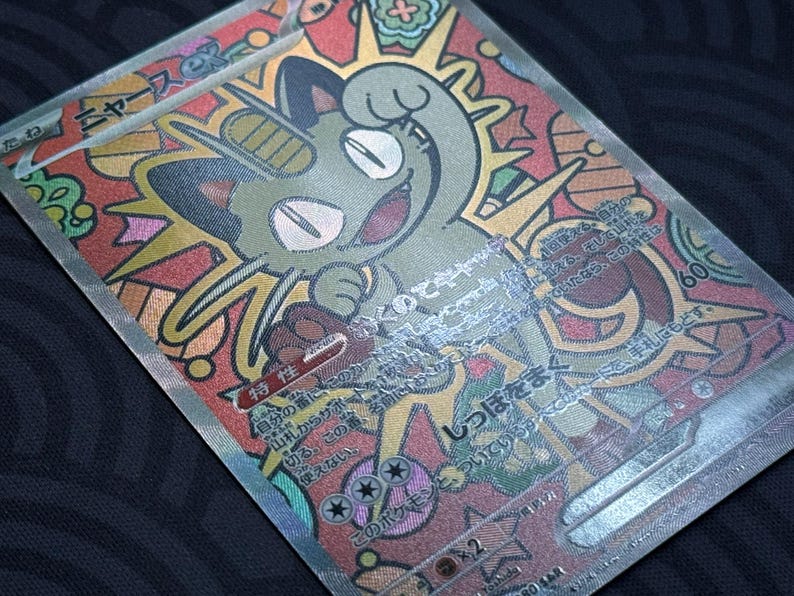 K&ouml;nnte beinhalten: Holografische Sammelkarte mit einer Cartoon-Katzenfigur in Gr&uuml;n mit einem l&auml;chelnden Gesichtsausdruck. Die Karte hat ein farbenfrohes Design im Glasmalerei-Stil, japanischen Text und die Zahl 60.