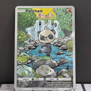 Puede incluir: Una carta coleccionable Pok&eacute;mon de Pancham, que representa una criatura parecida a un panda en un entorno forestal con una cascada. La carta tiene un ataque "Punch" y una debilidad de +20. La carta se muestra en un soporte transparente.