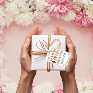 May include: A white gift box wrapped in twine with a gift tag that reads "Women like you make the world better." The gift tag has a colorful illustration of hands.