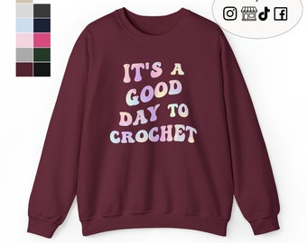 Puede incluir: Sudadera color burdeos con el texto "It's a good day to crochet" en letras arcoíris.