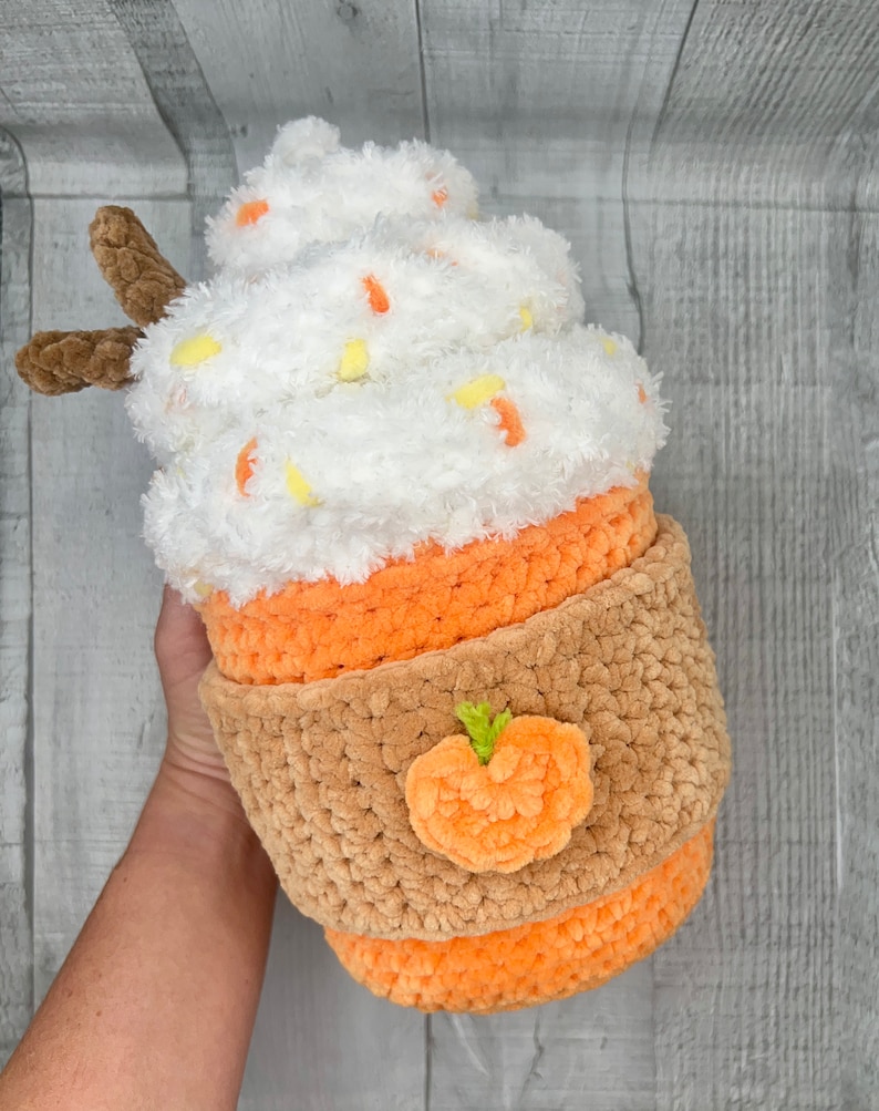 May include: A crocheted pumpkin spice latte plush toy with a white whipped cream top, orange and brown cup, and a small orange pumpkin on the side.