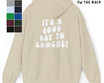 May include: A beige hoodie with a white graphic on the back that says "It's a good day to crochet" in a retro font.