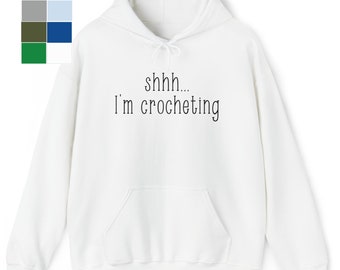 May include: White hoodie with a black text print that says "shhh... I'm crocheting"