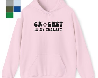 May include: Pink hoodie with a black graphic that says "CROCHET IS MY THERAPY" with a smiley face in the word "CROCHET".