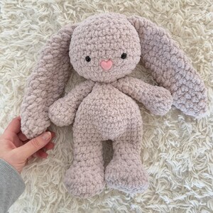 May include: A soft, crocheted plush bunny toy with long floppy ears. The bunny is light purple with a pink heart nose.