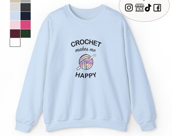 Puede incluir: Sudadera azul claro con el texto "CROCHET makes me HAPPY" y una bola de hilo de colores con un ganchillo.