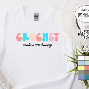 May include: White t-shirt with the text "CROCHET makes me happy" in a colorful retro font. The text is in pink, blue, and peach colors.