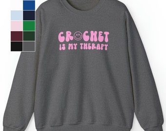 Puede incluir: Una sudadera gris oscura con el texto "CROCHET IS MY THERAPY" en rosa con una carita sonriente en el medio de la palabra "CROCHET".