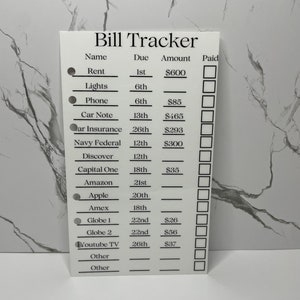 Può includere: Un tracker di fatture stampabile bianco con un titolo nero "Bill Tracker" e colonne per il nome, la data di scadenza, l'importo e il pagamento. Il tracker include fatture comuni come l'affitto, le luci, il telefono, il prestito auto, l'assicurazione auto, Navy Federal, Discover, Capital One, Amazon, Apple, Amex, Globe 1, Globe 2, Youtube TV e altre.