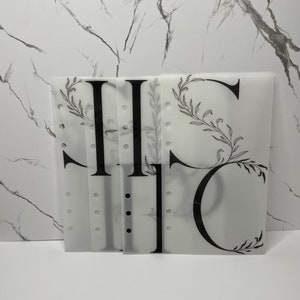 May include: Four clear plastic dividers with black lettering and a floral design. The dividers have holes along the left side for a binder.