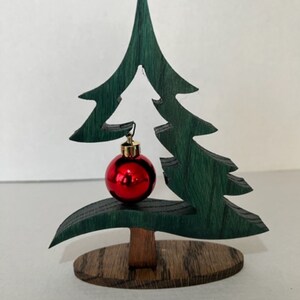 May include: A wooden Christmas tree ornament with a red and gold ornament hanging from it. The tree is green and has a brown base.