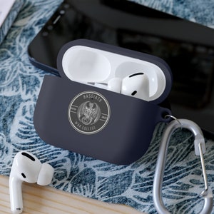 Op de afbeelding: Een donkerblauwe Airpods-hoes met een zilveren karabijnhaak. De hoes heeft een witte afbeelding van een draak met de tekst "Basgiath War College EstD 2023".
