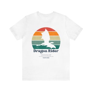 Puede incluir: Camiseta blanca con un diseño retro. Una silueta de dragón dentro de un círculo de puesta de sol. El texto "Dragon Rider" está debajo, con texto adicional del libro "Fourth Wing".