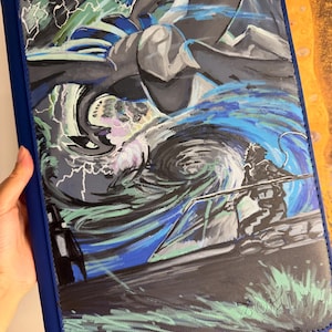 K&ouml;nnte beinhalten: Eine rechteckige blaue Dokumentenmappe mit einer detaillierten Illustration einer gro&szlig;en, dunklen, gefl&uuml;gelten Kreatur, die &uuml;ber einem wirbelnden blau-wei&szlig;en Strudel schwebt. Das Bild zeigt Blitze und die Silhouette einer Figur auf einer Plattform.