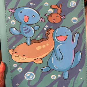 K&ouml;nnte beinhalten: Ein t&uuml;rkisfarbener Ordner mit einer gedruckten Illustration von drei blauen und braunen Wasserwesen, die zwischen wei&szlig;en Blasen schwimmen. Der Hintergrund hat ein wellenf&ouml;rmiges dunkelblaues Muster. Die Wesen umfassen eine kleine blaue Figur, eine braune und eine gr&ouml;&szlig;ere.