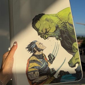 K&ouml;nnte beinhalten: Eine wei&szlig;e, rechteckige Dokumentenmappe mit einer detaillierten Comic-Illustration, die den gr&uuml;nen Hulk zeigt, wie er den gelb-blauen Wolverine anbr&uuml;llt, welcher seine metallischen Krallen aus den H&auml;nden ausgefahren hat.