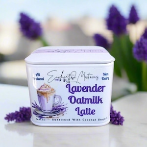K&ouml;nnte beinhalten: Wei&szlig;e Blechdose mit einem Design f&uuml;r einen Lavendel-Hafermilch-Latte. Der Text auf der Dose lautet "Enchanted Mixtures, All Natural, Non Dairy, Lavender Oatmilk Latte, Sweetened with Coconut Sugar".
