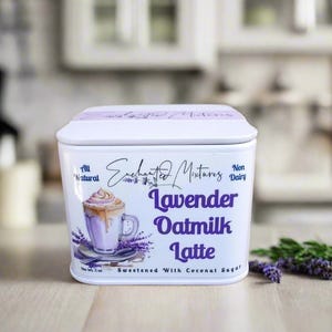 K&ouml;nnte beinhalten: Wei&szlig;e Blechdose mit einer Illustration von einem Lavendel-Hafermilch-Latte. Der Text auf der Dose lautet "Enchanted Mixtures, All Natural, Non Dairy, Lavender Oatmilk Latte, Sweetened with Coconut Sugar".